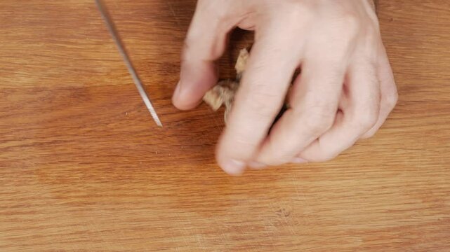 A cook cuts morel mushrooms into small pieces using a knife on a wooden cutting board. Close-up.