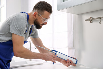 Worker with caulking gun sealing countertop indoors