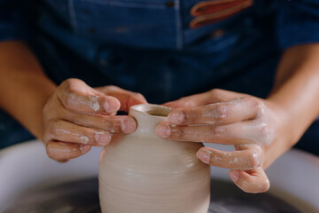 Close-up of a Latina woman’s hands shaping a ceramic piece in her workshop. The image captures...