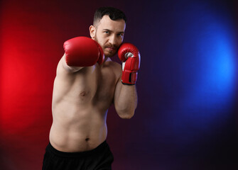 Man with boxing gloves fighting on dark background in neon lights, space for text