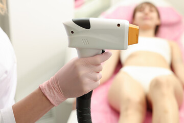 Professional cosmetologist holding laser depilator near patient in beauty salon, closeup