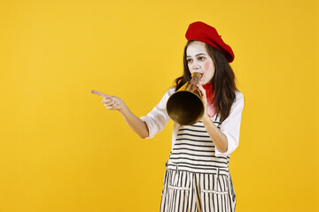 Cute girl dressed like mime with megaphone pointing at something on yellow background, space for...