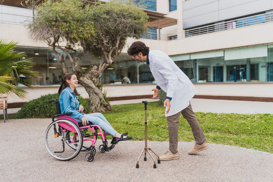 Smiling doctor interacting with young woman in wheelchair outdoors - Doctor talking with young woman with cerebral palsy in a wheelchair outside a healthcare facility - Concept of cerebral palsy.