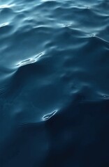 Naklejka premium Vertical top view of dark blue water surface with light reflections, ripples creating a calm, abstract background. Deep water texture wave pattern. Natural marine backdrop.