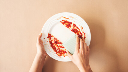 Woman using green cleaning sponge to clean up and washing food stains and dirt on white dish after...