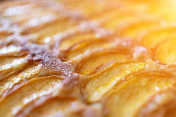 A close up of a dessert made of sliced peach. The dessert is covered in a caramel glaze and has a golden brown crust. The peach are arranged in a spiral pattern, creating a visually appealing