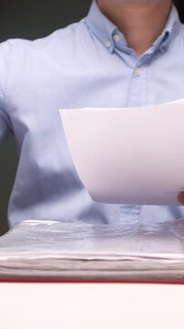 vertical video Office worker stapling papers at desk with laptop and files