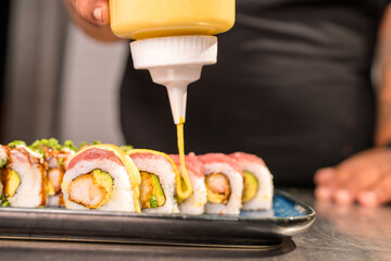 Chef pouring sauce on delicious maki sushi rolls in a restaurant