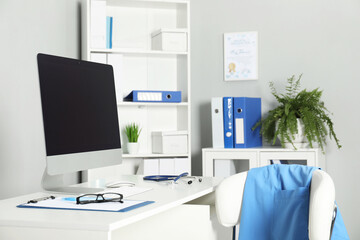 Doctor's workplace. Computer monitor, clipboard, stethoscope and glasses on white table in medical office