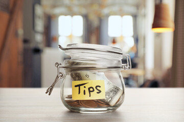 Tips jar with money on light wooden table in cafe