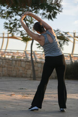 Active middle-aged woman doing stretching and jogging outdoors at sunset