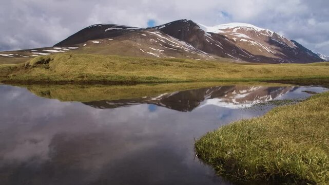 This 4K drone footage captures a peaceful lake in Arabel Plateau, Kyrgyzstan, surrounded by lush greenery, snowy mountain peaks, and perfect reflections of nature&rsquo;s vibrant colors