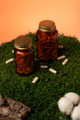 Herbal supplement capsules in amber jars on moss background. The warm orange background enhances the natural and organic feel, for themes related to health, wellness, vitamins, and natural remedies
