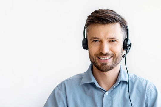 Portrait of smiling male customer service operator in headset posing at workplace, looking at camera, portrait of handsome hotline manager sitting at desk with laptop in white office, copy space