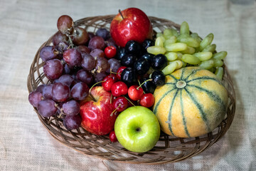 Assortment of juicy fruits red apple, green apple, red grapes, green grapes and musk melon on the fruit basket against dark background