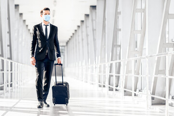 Businessman with luggage going on business trip, wearing face mask at the airport, copy space