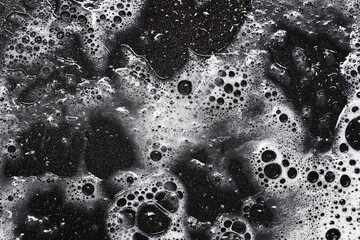Black foam bubbles. Soap and water texture. Abstract foam surface. Cleaning background. Liquid bubbles closeup. Dark wet surface. Car wash detail. Soap suds pattern. Shiny foam texture.