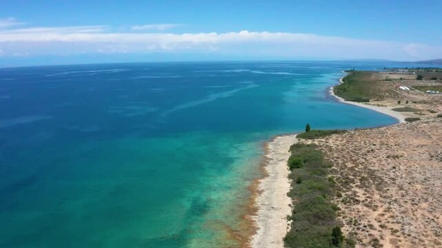 This stunning drone footage captures the crystal-clear blueish-green waters of Assyk Kul Lake, with sandy shores and lush greenery surrounding the water in Kyrgyzstan.