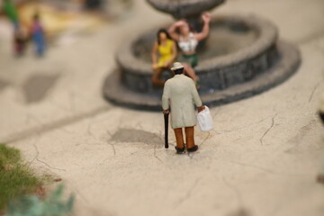 Senior mit Gehhilfe beobachtet zwei Frauen an einem Brunnen