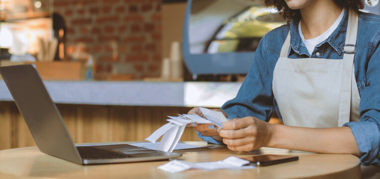 Financial difficulties and problems of small businesses during covid-19 lockdown. Millennial african american woman owner manager in apron works with account and bookkeeping in cafe, panorama, cropped