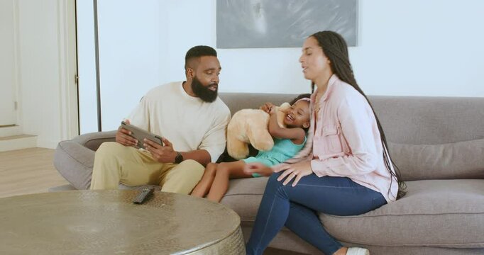Diverse family announcing sibling surprise in cozy living room with tablet and teddy bear