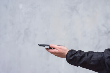 A man in a black jacket holding a smartphone against a gray concrete wall. Modern technology and the use of mobile devices.