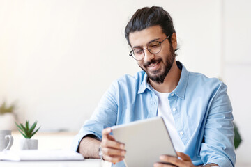Arab Freelancer Guy Using Digital Tablet At Home, Having Break In Work, Sitting At Desk, Browsing...