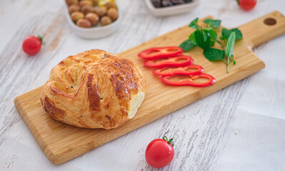 Golden puff pastry with fresh ingredients. Baked golden puff pastry is on a wooden cutting board. Surrounded by red bell pepper slices, cherry tomatoes and fresh herbs. Selective focus.