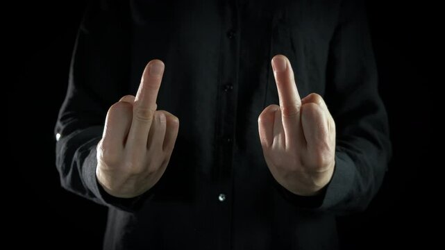 Man with fuck you' gesture indoor. A view of man hands with angry feelings show fuck you gesture against black background.