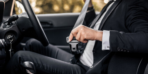 Driving safety concept. Unrecognizable businessman fasten seat belt in his car, ready to go to office. Man in stylish suit putting on his seatbelt before driving car to airport, cropped
