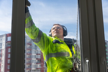 A Dedicated Window Cleaner Practicing Safety While Cleaning Glass on a High-Rise Building with a Vibrant Cityscape in the Background Under a Clear Blue Sky © Viktoriia