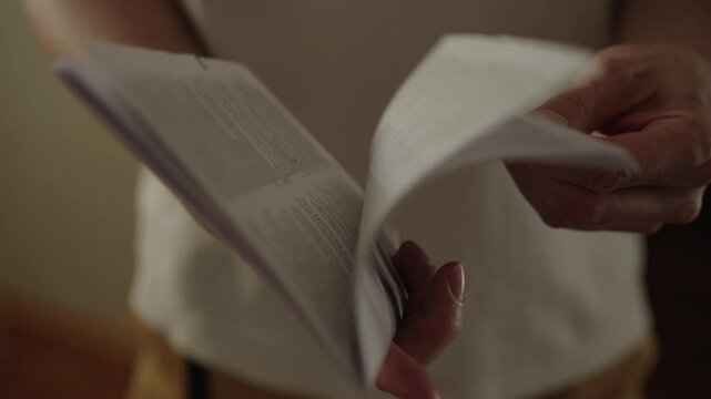Close-up of unrecognizable man turning pages of instruction manual reading information. Closeup of male hands guiding paper as absorbs information in home setting. Shooting in slow motion.