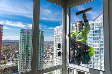 Professional Window Cleaner Working at Heights in an Urban Setting with a Scenic View of High-Rise Buildings in the Background and a Clear Blue Sky Above, Showcasing Modern Cleaning Techniques © Viktoriia
