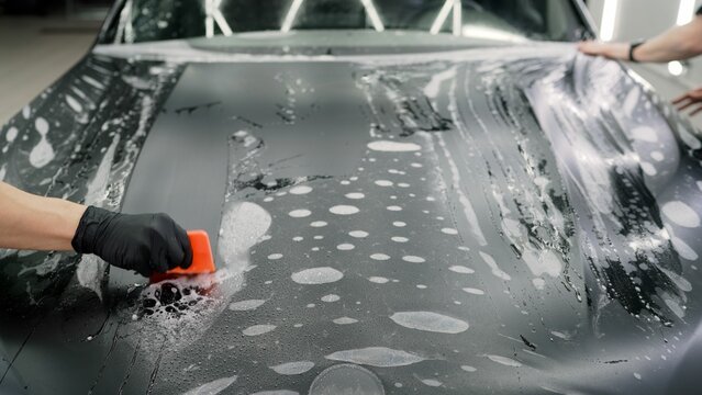 Professional installing protective film on car hood using squeegee and soap solution