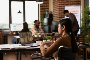 Female business leader in a wheelchair engages in a video conference with potential investors from her desk. Asian female manager holds a virtual discussion with her remote colleagues.
