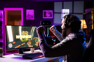 Esports player playing videogames in front of subscribers during livestream, celebrating after...