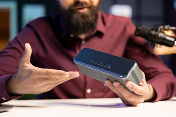 Man doing technology review of wireless portable speaker for internet vlogging channel. Close up shot of music playing device held by influencer showing it to his subscribers