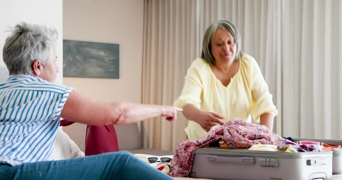 Diverse senior friends packing for girls trip indoors with colorful suitcase and glasses
