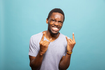 Excited young black man standing and making rock and roll gesture against an isolated background....