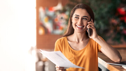 Young arab girl discussing project with client on phone, working with laptop at cafe, copy space