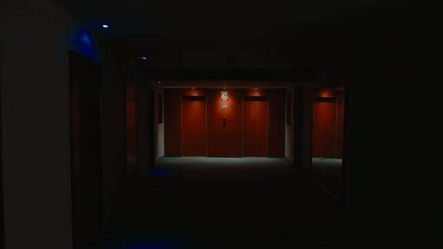 Dark, empty corridor revealing red elevator doors at night, camera gradually zooming closer to call button, creating suspenseful and mysterious atmospheric scene with dramatic shadowy lighting