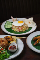 Traditional Indonesian Fried Rice with Sunny-Side-Up Egg, Cucumber Slices, and Krupuk on Banana Leaf