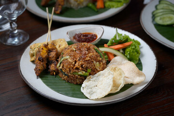 Indonesian Fried Rice with Satay, Fried Egg, and Fresh Vegetables on Banana Leaf