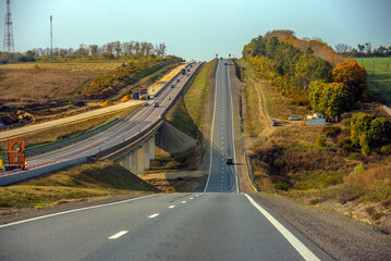 a section of highway running along a hill. On the left, construction or widening work can be seen - machinery, sand embankments and temporary barriers.  