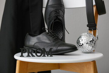Word PROM with male shoes, blazer and disco ball on chair against white background