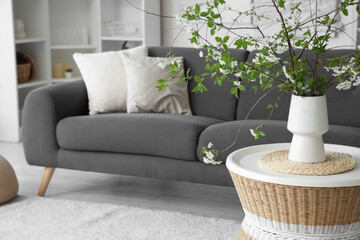 Vase with blooming branches on table in living room