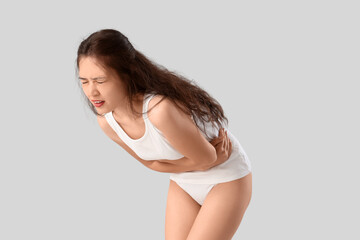 Young Asian woman in underwear suffering from menstrual pain on light background