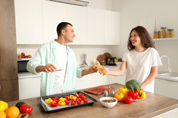 Young couple with sunflower oil cooking bell peppers in kitchen
