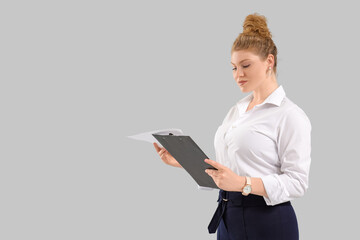 Young beautiful businesswoman in formal clothes with clipboard on grey background