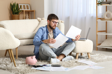 Fototapeta premium Young man in debt with papers sitting on floor at home